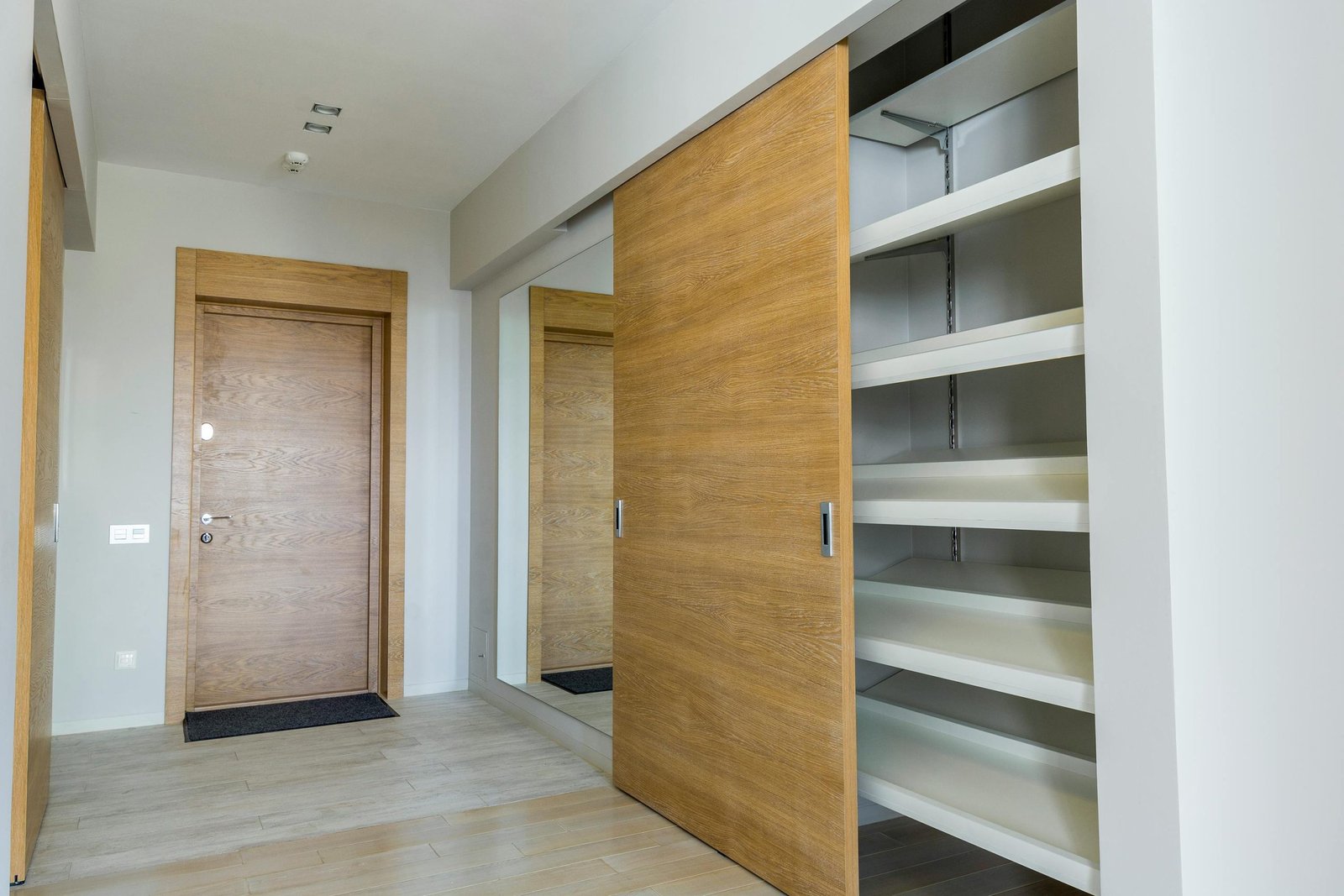 Elegant modern walk-in closet with wooden sliding door and empty shelves in a sleek minimalist style.