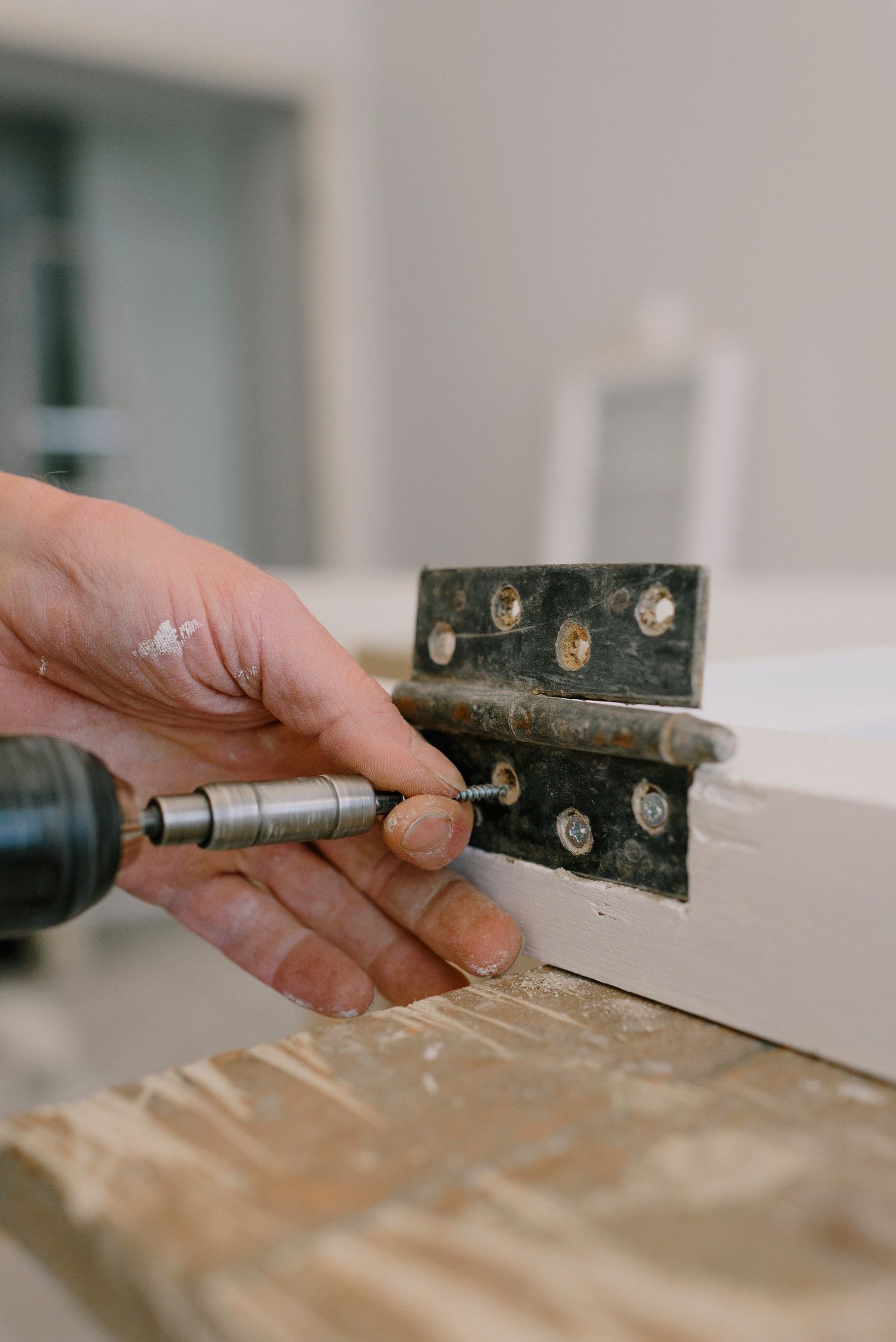 Hand screwing a door hinge into a frame with a drill