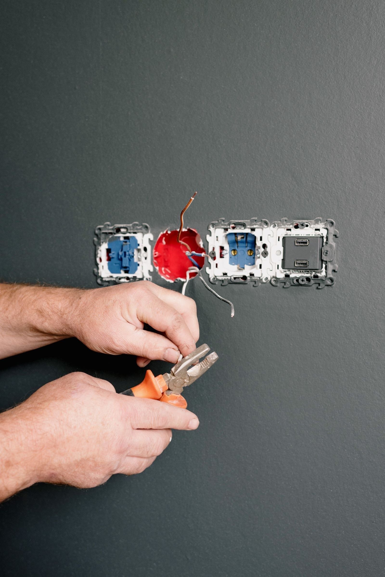 Hands using pliers on wiring at wall sockets