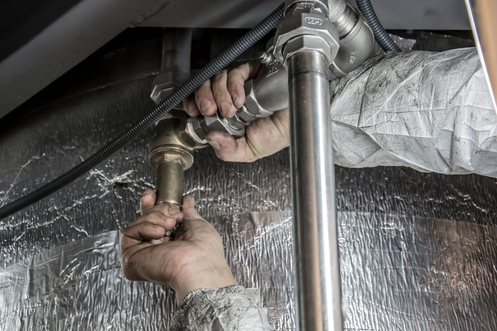 Hands fitting a brass pipe joint under a sink
