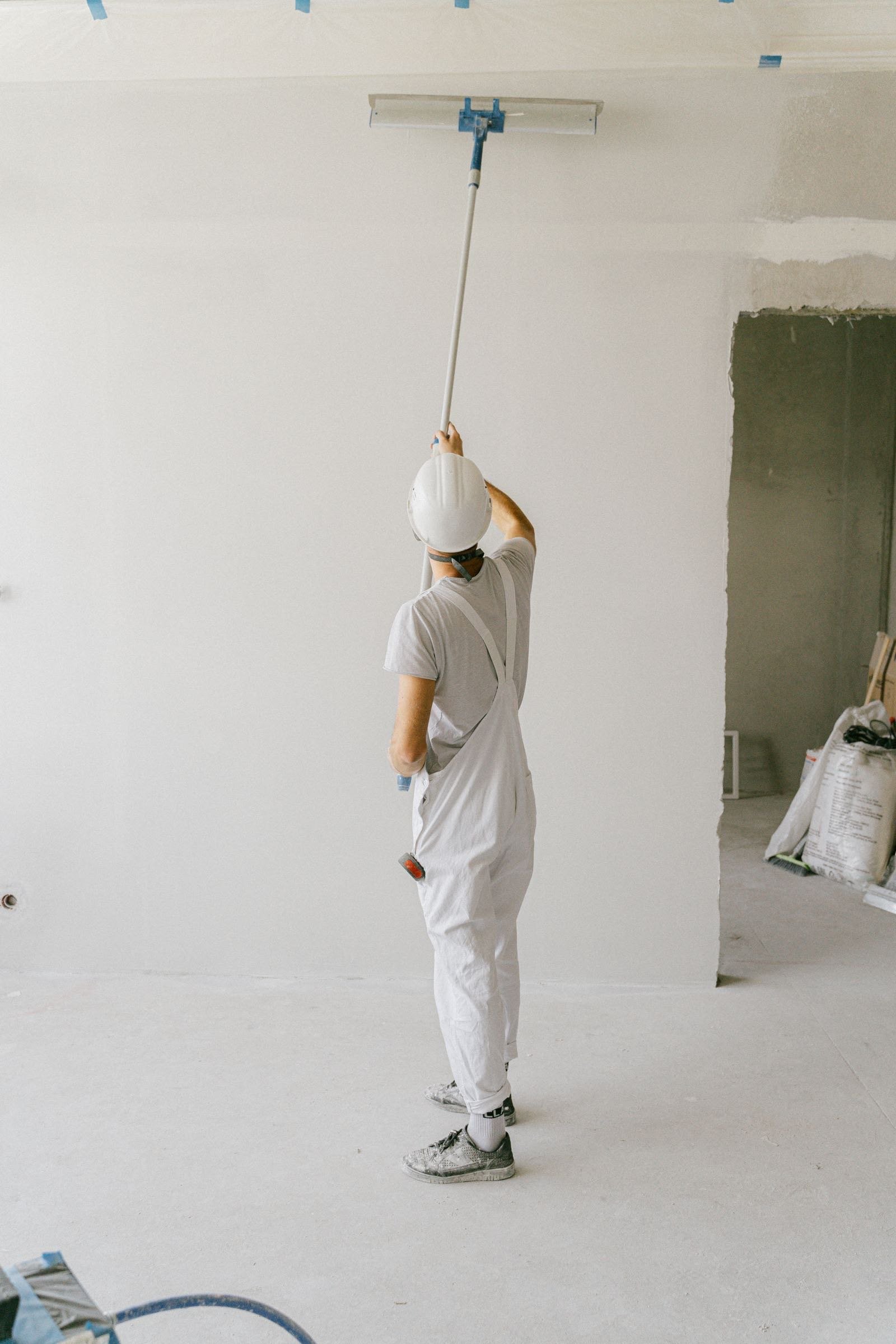 Worker in overalls and a hard hat smoothing a ceiling
